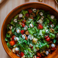 A bowl of bruschetta salad with balsamic drizzle on a wooden board.