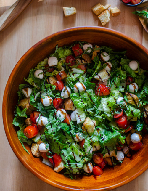 A bowl of bruschetta salad with balsamic drizzle on a wooden board.