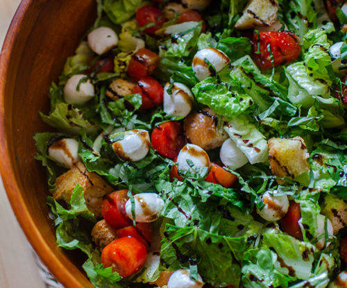 Bruschetta salad in a wooden salad bowl with balsamic glaze drizzled on top.