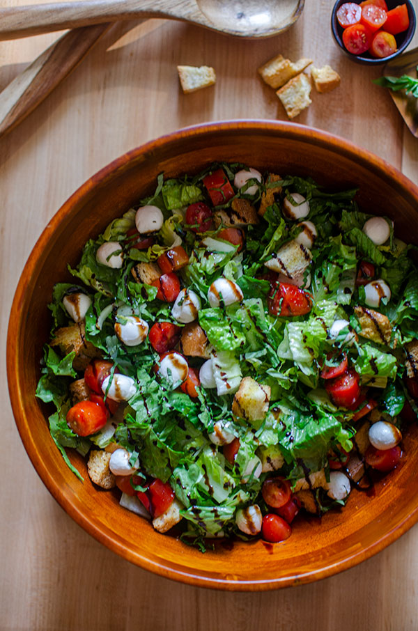 A bowl of bruschetta salad with balsamic drizzle on a wooden board. 