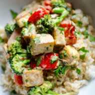 Closeup of tofu stir fry on top of brown rice in a white bowl