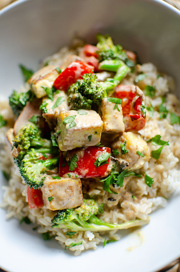 Closeup of tofu stir fry on top of brown rice in a white bowl