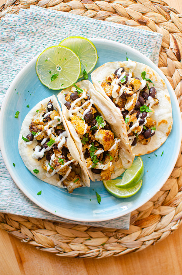 Long shot of three tacos on a blue plate with limes on a blue and white napkin