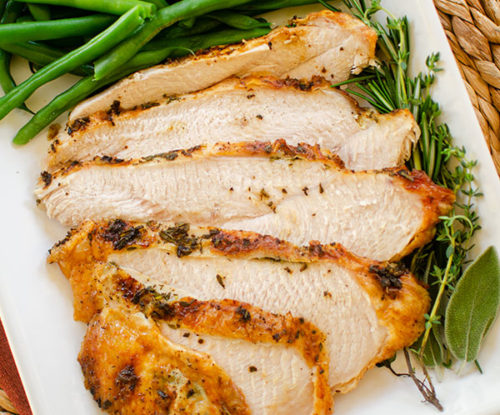 Slices of turkey breast on a platter with fresh herbs, green beans and stuffing.