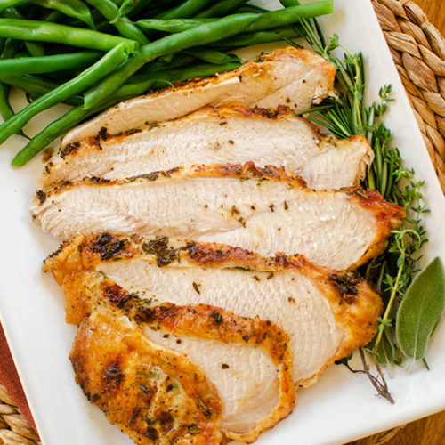Slices of turkey breast on a platter with fresh herbs, green beans and stuffing.