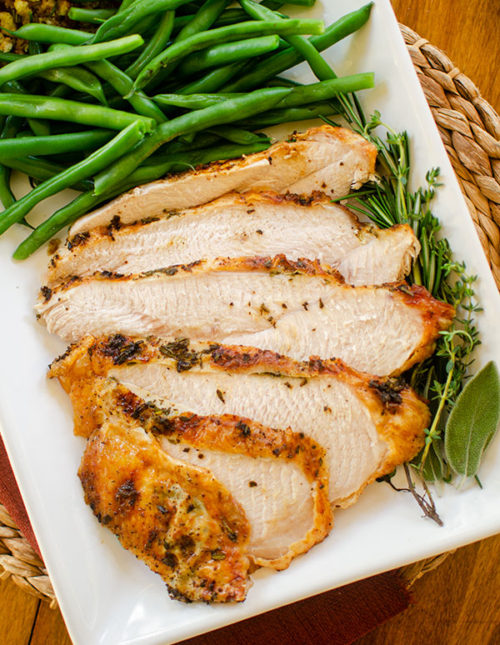Slices of turkey breast on a platter with fresh herbs, green beans and stuffing.