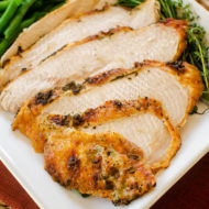 Closeup of sliced turkey breast on a white platter with green beans and fresh herb garnish.