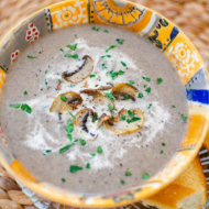 Cream of mushroom soup in an orange bowl with cream and satueed mushrooms on top.