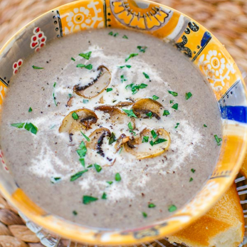 Cream of mushroom soup in an orange bowl with cream and satueed mushrooms on top.