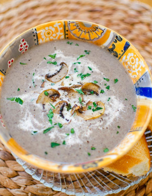 Cream of mushroom soup in an orange bowl with cream and satueed mushrooms on top.