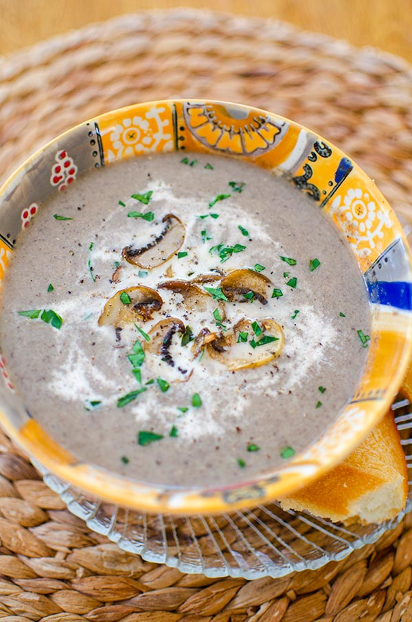 Cream of mushroom soup in an orange bowl with cream and satueed mushrooms on top.