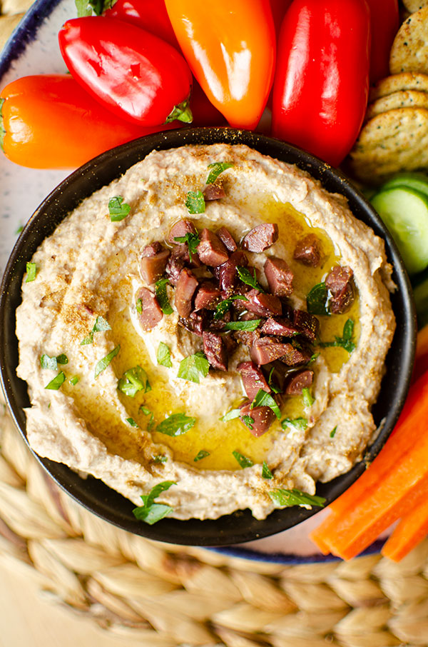 Closeup of olive hummus in a bowl with a platter of vegetables and crackers.