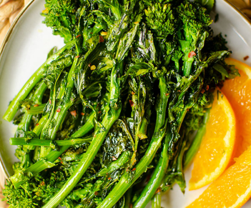 Roasted broccoli rabe on a plate with sliced oranges