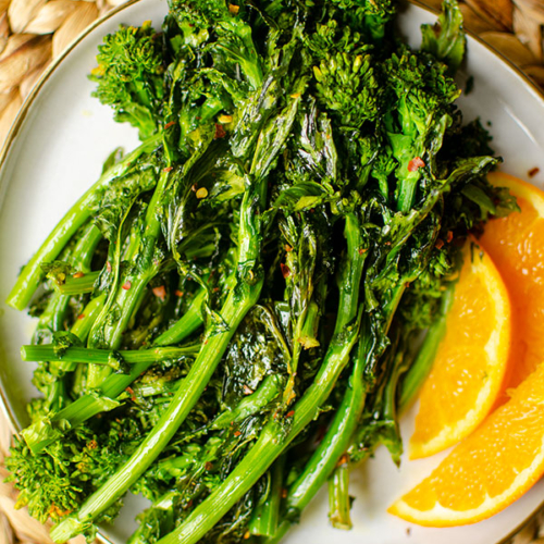 Roasted broccoli rabe on a plate with sliced oranges