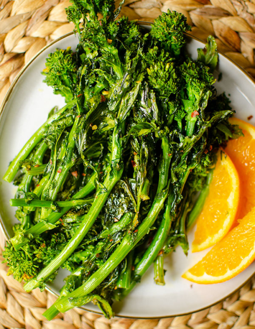 Roasted broccoli rabe on a plate with sliced oranges
