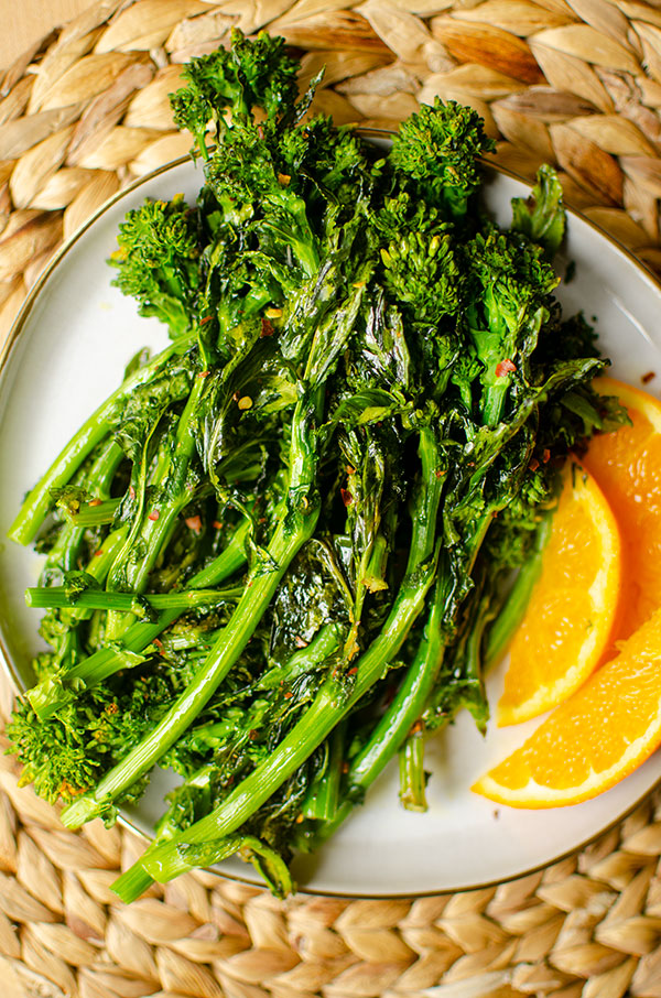 Roasted broccoli rabe on a plate with sliced oranges