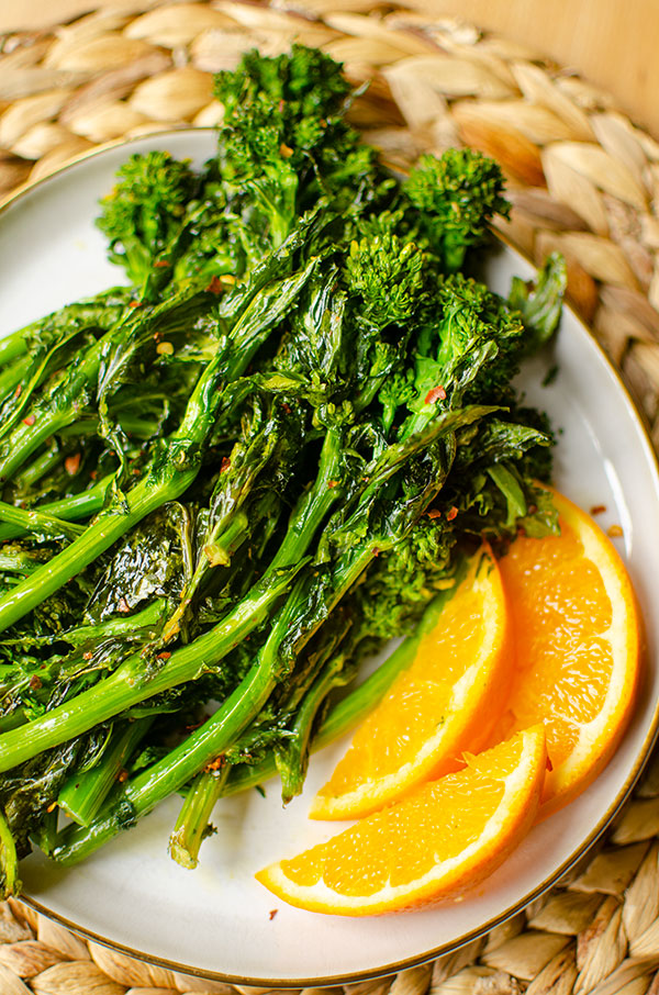 Closeup of roasted borrocoli rabe on a plate with slices of orange