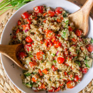 A big bowl of quinoa salad on a placemart with parsley and tomato.