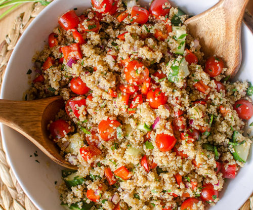 A big bowl of quinoa salad on a placemart with parsley and tomato.