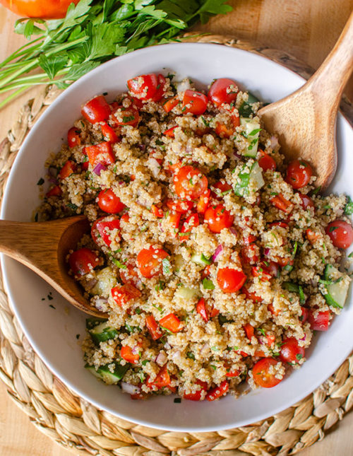 A big bowl of quinoa salad on a placemart with parsley and tomato.