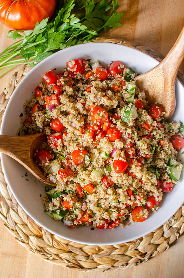 A big bowl of quinoa salad on a placemart with parsley and tomato.