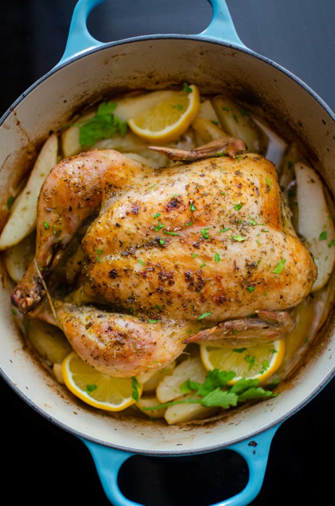 A cooked crispy roasted whole chicken in a turquoise Dutch oven 