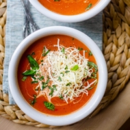 Closeup of instant pot tomato soup in a white bowl with cheese and basil on top.