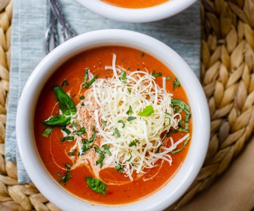 Closeup of instant pot tomato soup in a white bowl with cheese and basil on top.
