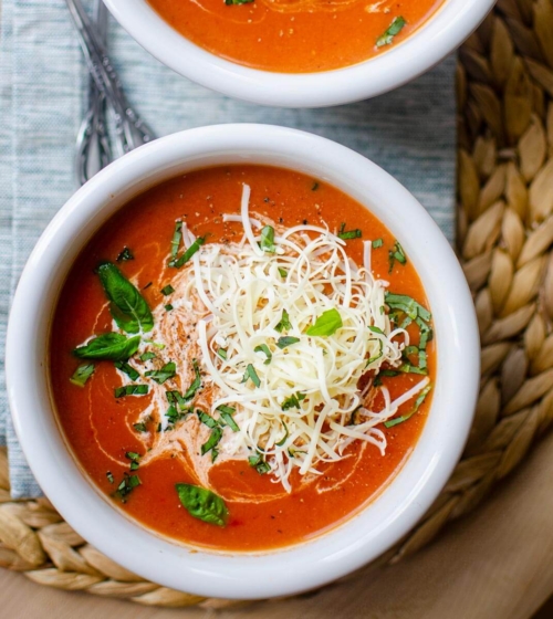 Closeup of instant pot tomato soup in a white bowl with cheese and basil on top.