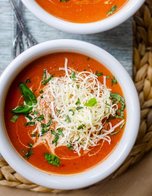 Closeup of instant pot tomato soup in a white bowl with cheese and basil on top.