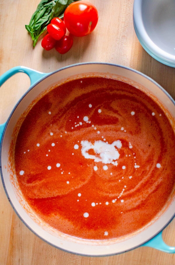 A pot of tomato soup with a drizzle of heavy cream
