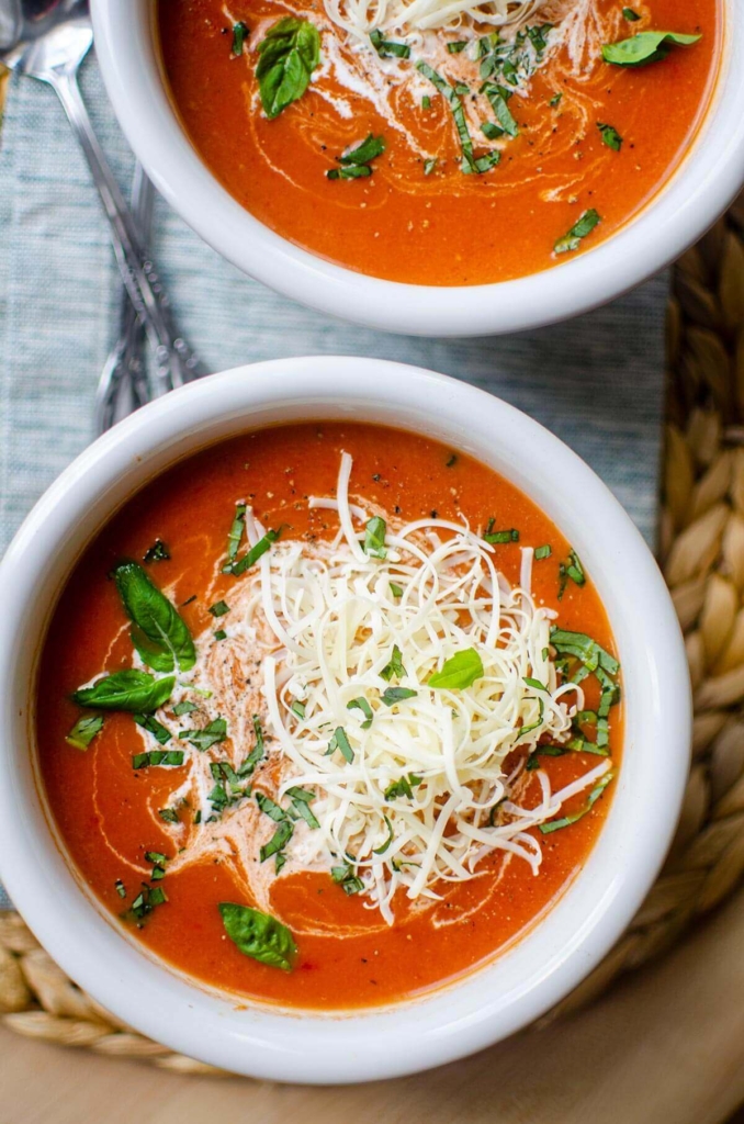 A bowl of tomato soup with cheddar and basil on top