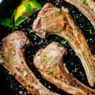 Closeup of finished lamb in a cast iron with parsley and lemon for garnishes