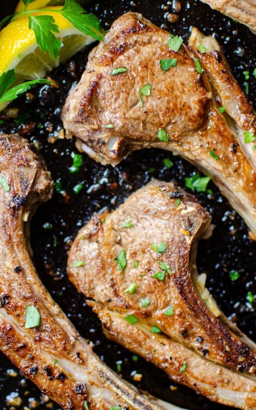 Closeup of finished lamb in a cast iron with parsley and lemon for garnishes