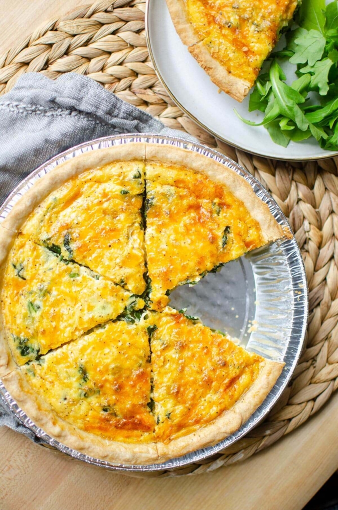 Quiche cut into slices in a pie plate with one serving missing