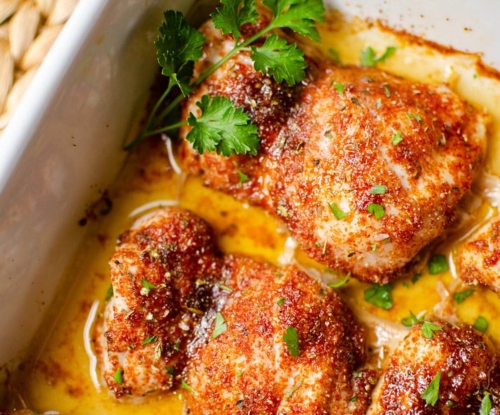 Closeup of cooked chicken thighs in a white casserole dish.