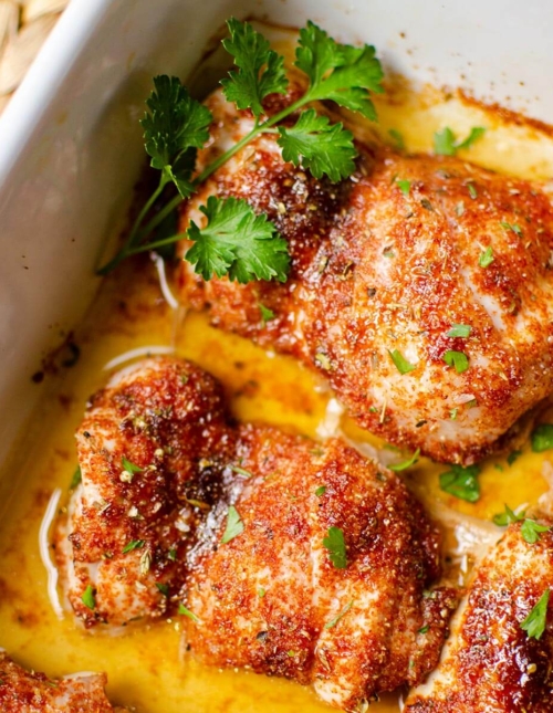 Closeup of cooked chicken thighs in a white casserole dish.