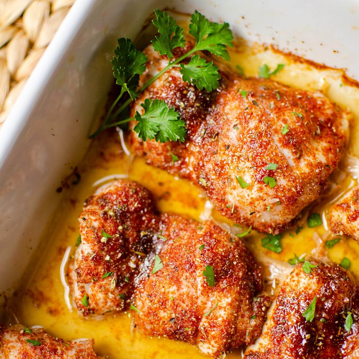 Closeup of cooked chicken thighs in a white casserole dish.