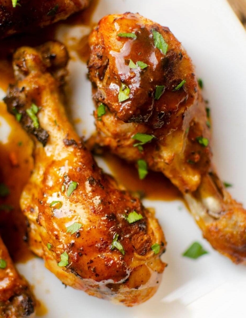 Close up of drumsticks on a plate with gravy and sprinkled with parsley.