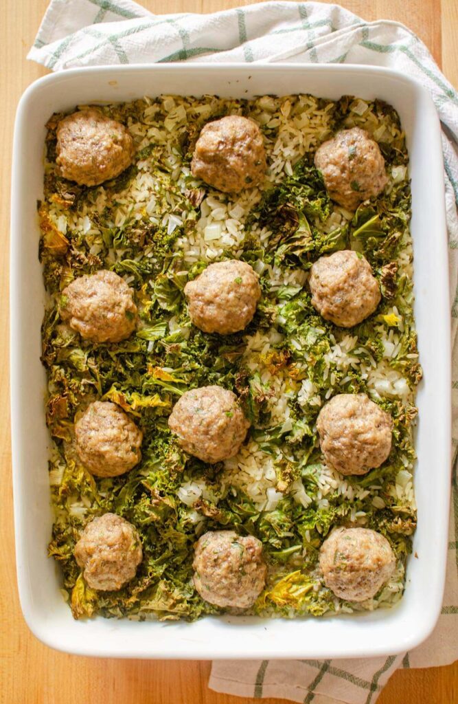 Baked meatballs and rice with kale in a white 9x13 dish.