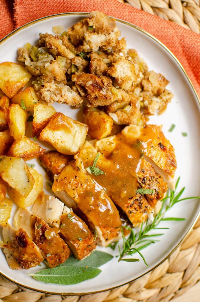 A serving of sliced chicken with roast potatoes and stuffing with gravy and fresh herbs.