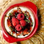 Baked brie in red brie baker with raspberries and balsamic glaze on top.