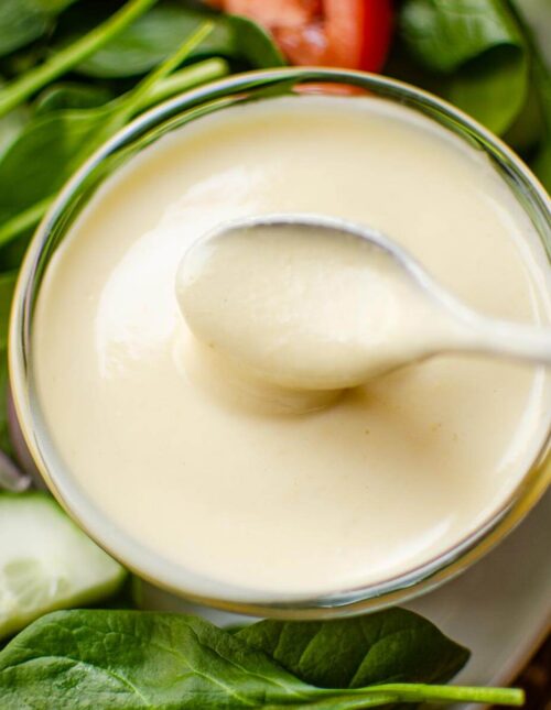 Closeup of a spoon in the dressing with a salad on the side.