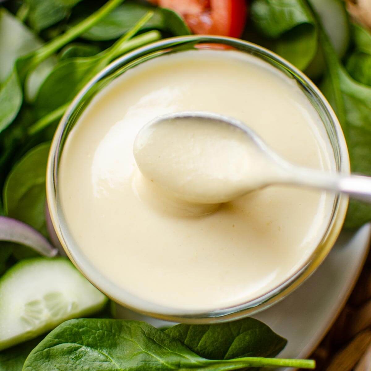 Closeup of a spoon in the dressing with a salad on the side.