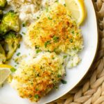 Closeup of cooked cod fillets on a white plate with broccoli and lemon.