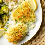 Closeup of cooked cod fillets on a white plate with broccoli and lemon.