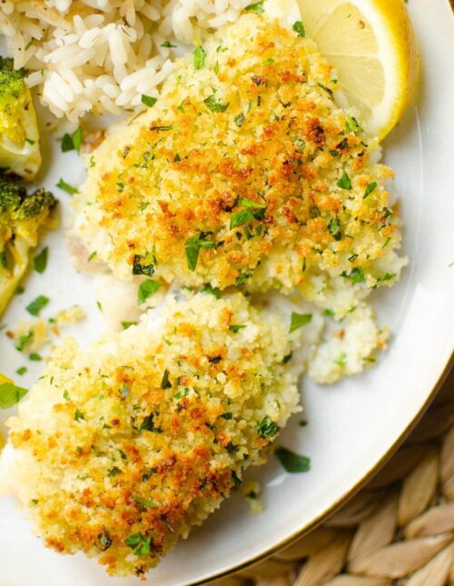 Closeup of cooked cod fillets on a white plate with broccoli and lemon.