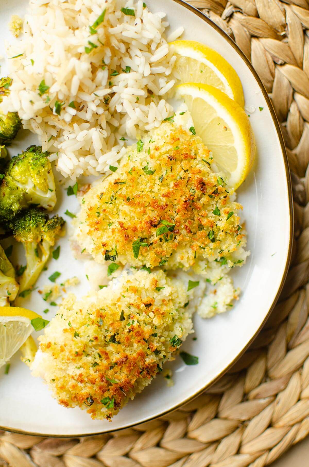 A plate of cod, rice and broccoli with slices of lemon.