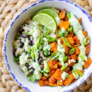 Closeup of a serving of sweet potato bowl with avocado crema and lime slices in a white bowl with a blue border.