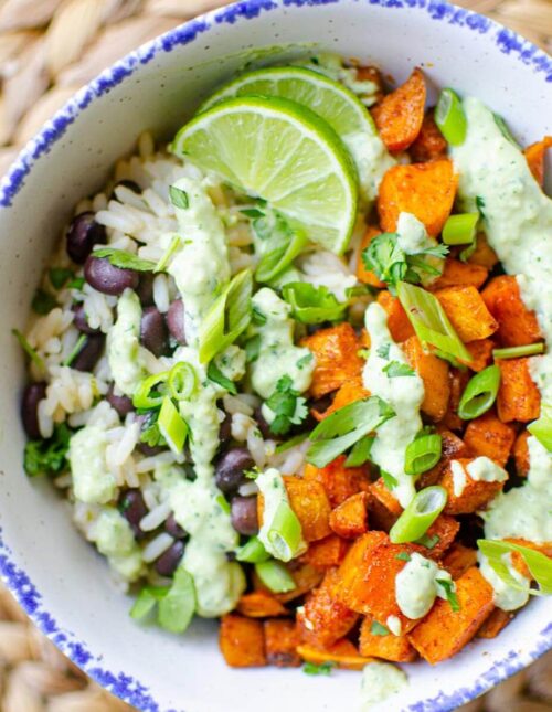 Closeup of a serving of sweet potato bowl with avocado crema and lime slices in a white bowl with a blue border.